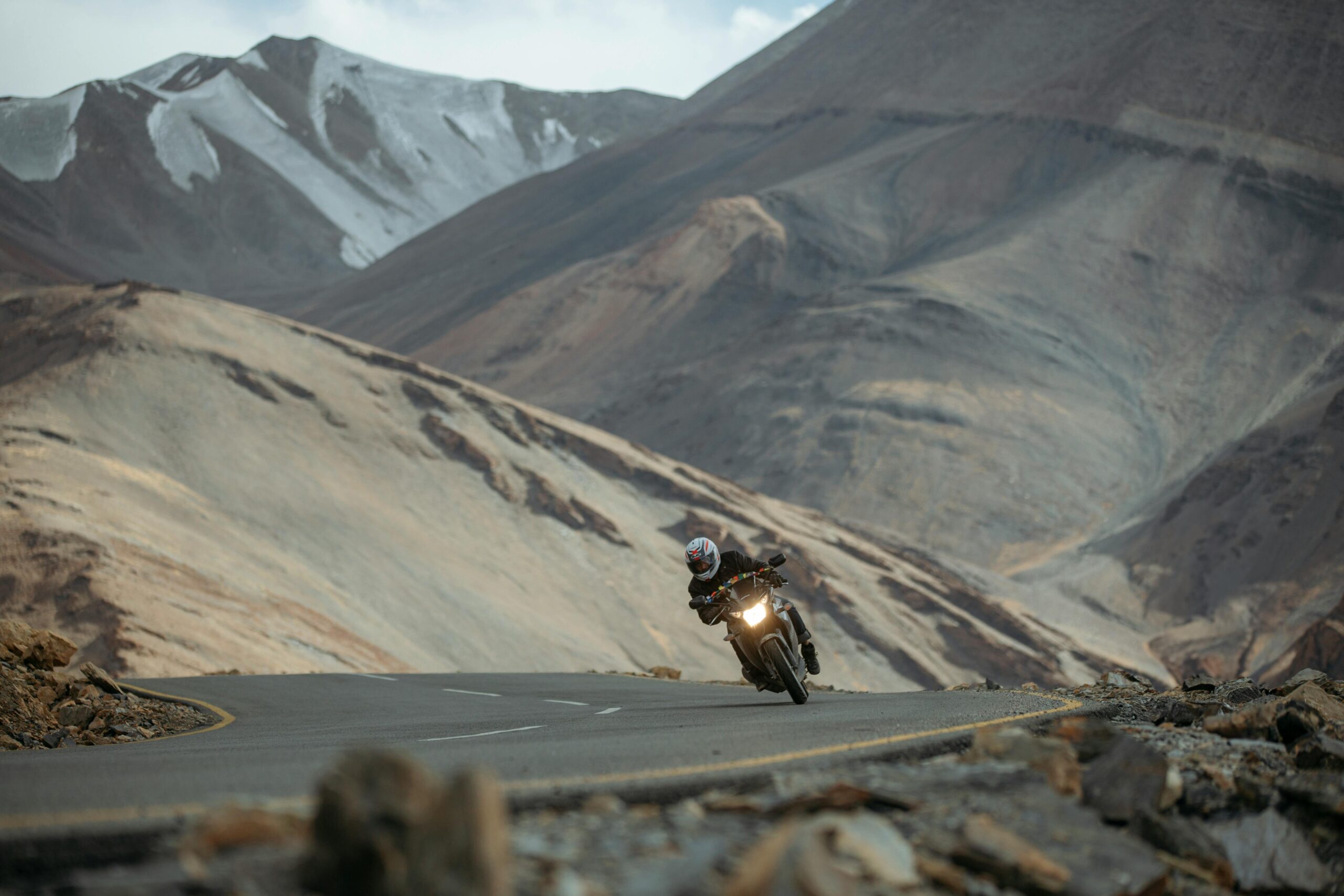 Motorcyclist navigating a winding road amid the stunning landscape of the Ladakh mountains in India.