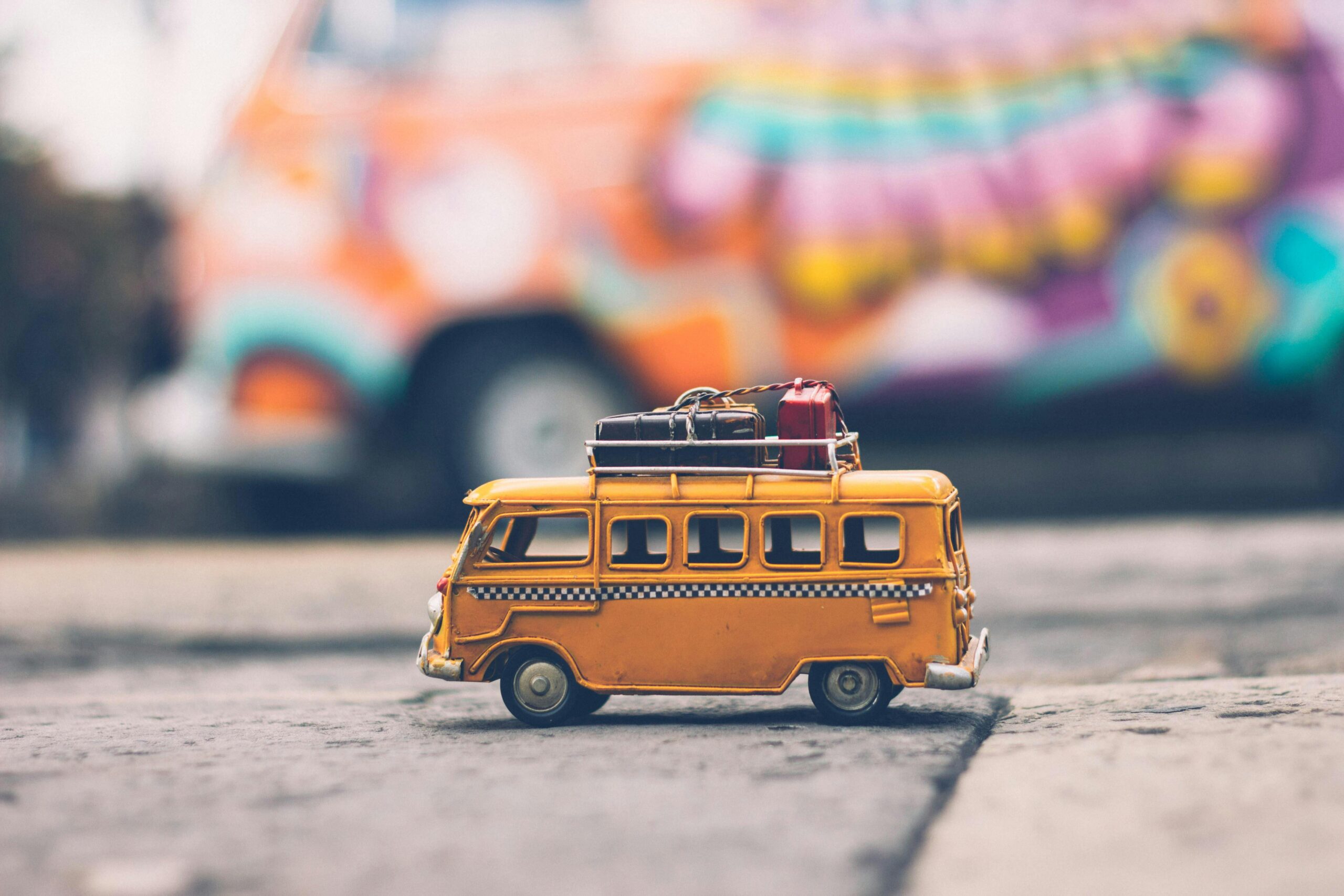 ABOUT Close-up of a toy Volkswagen van with luggage, set against a colorful street backdrop, evoking summer travel vibes.